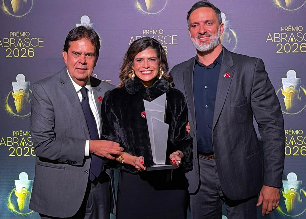 Três pessoas posam sorrindo com um troféu no Prêmio Abrasce 2026, diante de fundo roxo com o texto do evento.