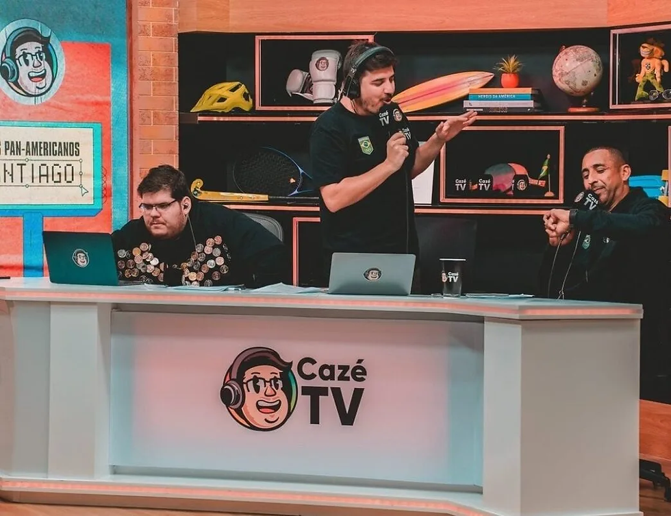 Três comentaristas no estúdio do Cazé TV, com fones e microfones, falam animados atrás de mesa branca com logo.
