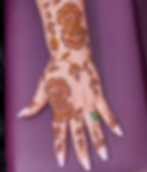 A hand adorned with a beautiful, intricate henna design, placed on a rich purple background.