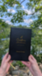 A Creative's Journal held up in front of trees and water