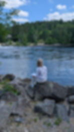Author Catherine McCallum sitting on a rock by the water with A Creative's Journal