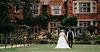 Bride and groom walking hand in hand across the gardens at Moxhull Hall, with the ivy-covered red brick manor house creating a picturesque backdrop for their wedding day.