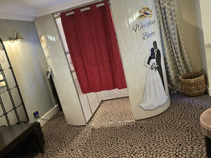 Oval Fun Booth wedding photo booth set up at a wedding reception, featuring a cream vintage-style booth with wedding graphics and a red curtain backdrop.