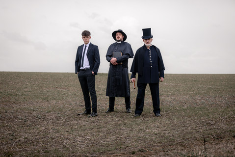 Group portrait of male authority figures in period costume standing in a barren landscape.