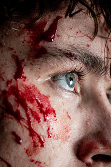 Extreme close-up of male model’s eye with splattered red makeup resembling blood, psychological fashion photography