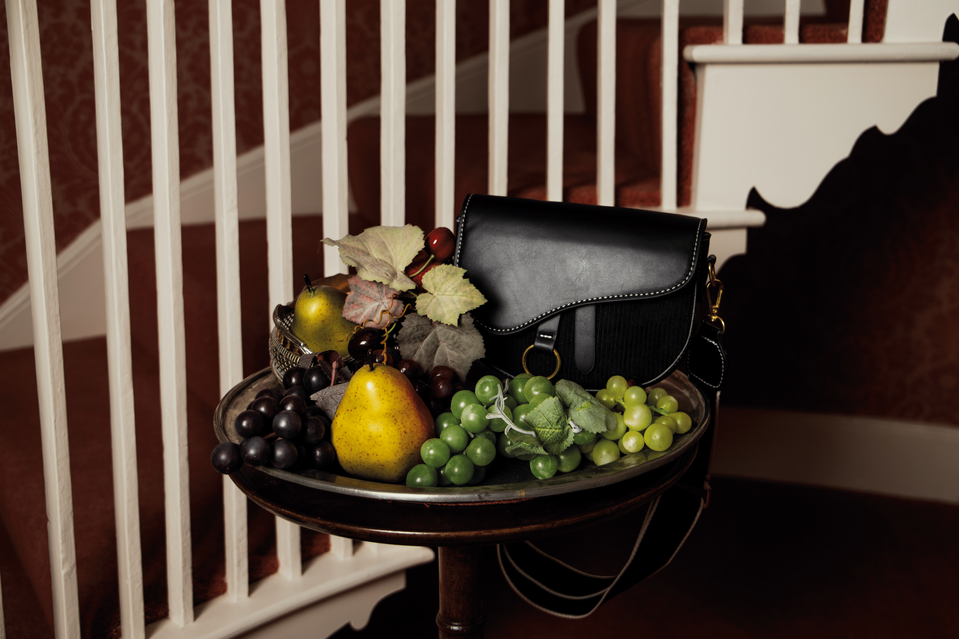 Still life editorial photograph of a leather handbag and fruit arrangement on a vintage side table.