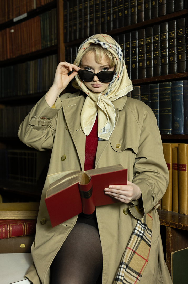 Fashion portrait of a model wearing a headscarf and tailored coat in a library setting for dissertation imagery.