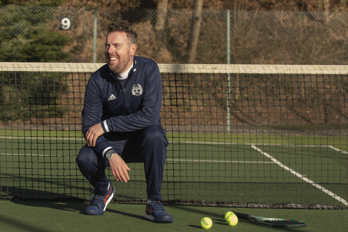 Candid shot of coach Kirk Woodall laughing on a tennis court, emphasizing the friendly and engaging nature of the coaching brand.