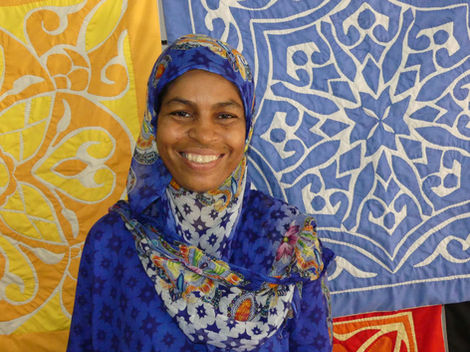 Aida surrounded by the needlework work of Sasik Women's Cooperative, Zanzibar.
