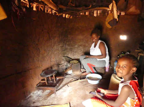 Inside a traditional mud and sticks kitchen and food store with two girls cooking on a small traditional stove