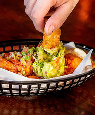 A hand dipping a chicken wing into sauce