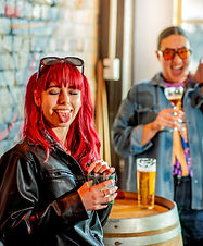 A lady with bright red hair sticking tongue out while holding a pint glass.