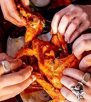 Hands grabbing a spicy chicken wing from the bowl.