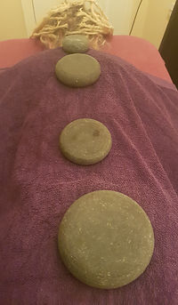 a person lying on the couch face down with a towel over them an four large basalt stones placed on her back. These are left there whilst the massage is continued on the legs.