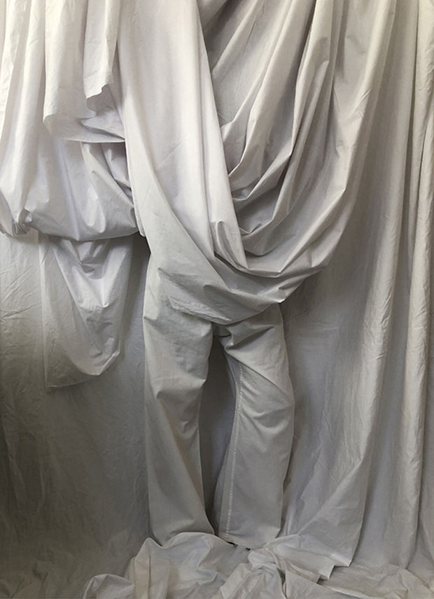 Feelings of being invisible expressed with person wearing white cotton trousers stood in camouflage behind a large white draped cotton sheet