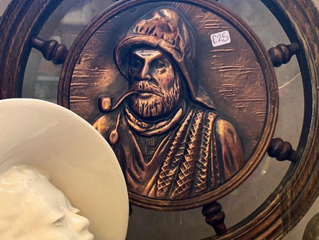 Bronze nautical plaque with sailor emits rustic vibe; white ceramic face with £20 tag in foreground, brass vase right, £25 tag on plaque.