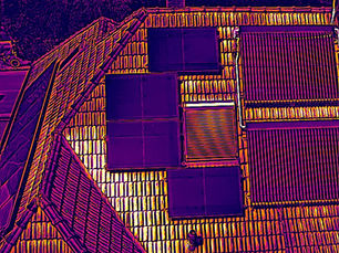 Thermografisches Infrarot-Wärmebild einer Solaranlage auf einem Dach. Die Photovoltaik-Module und Solarthermie-Kollektoren zeigen eine homogene, fehlerfreie Temperaturverteilung ohne Hotspots, während die umliegenden Dachpfannen durch die Sonne stark erhitzt sind.