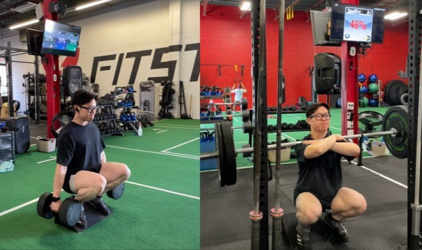 Person squatting in a gym, holding dumbbells on the left and a barbell on the right. Green turf and red walls in the background. Trying to make progress at the Gym.