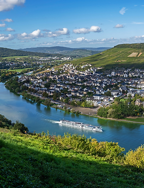 Riverside luxury cruise ship sailing through scenic European river valley with green hillside village on river cruise trip