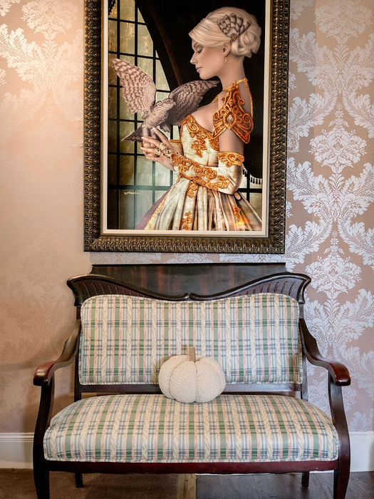 Framed art of a woman holding a bird above a plaid settee