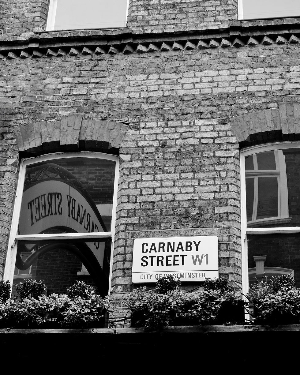 Black and white photo of a Carnaby Street W1 sign on a brick wall, featuring a reflection of the arched street sign in window