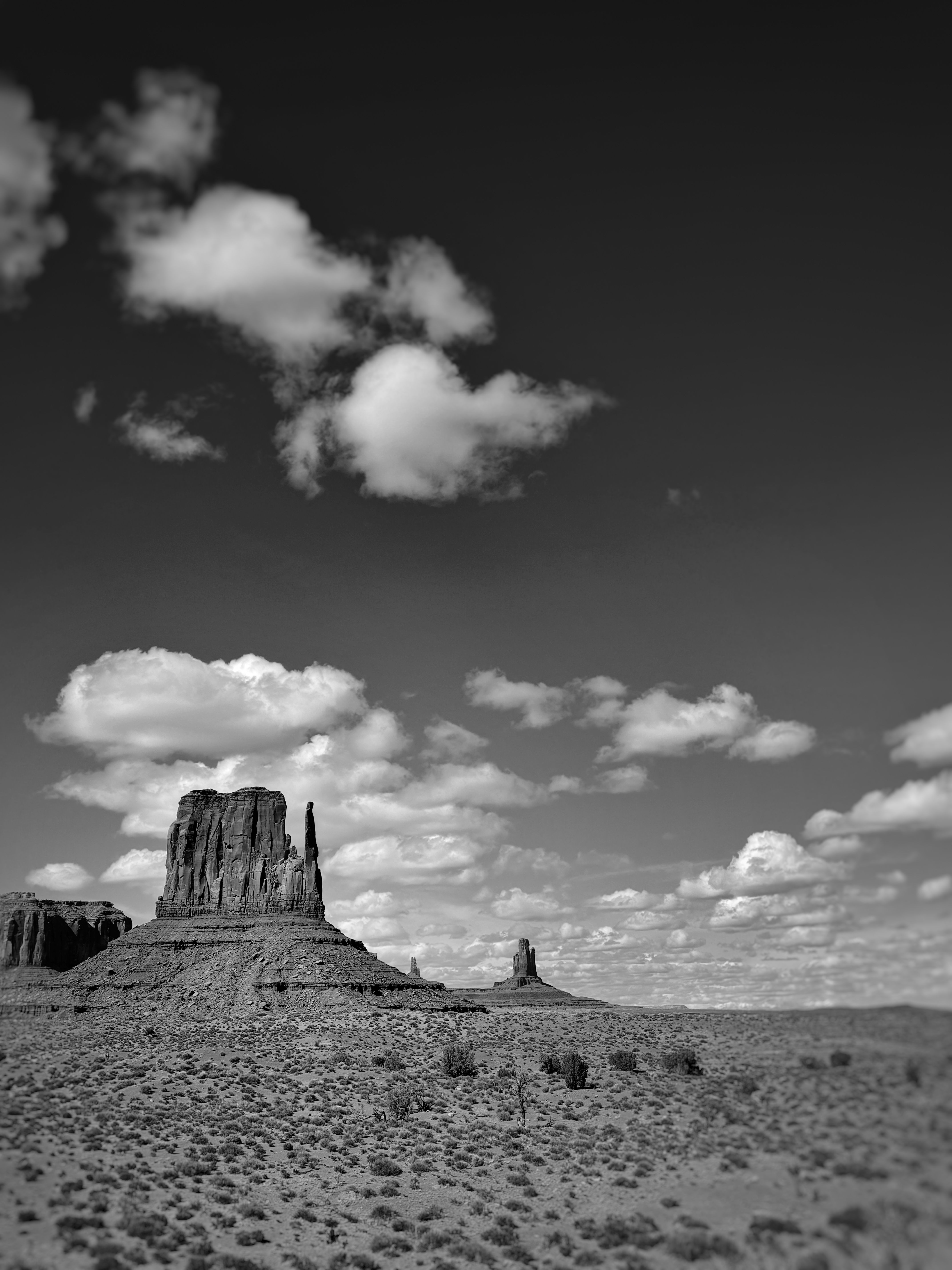 Black and white photo print of rock formations amongst clouds in sky in Monument Valley, Arizona