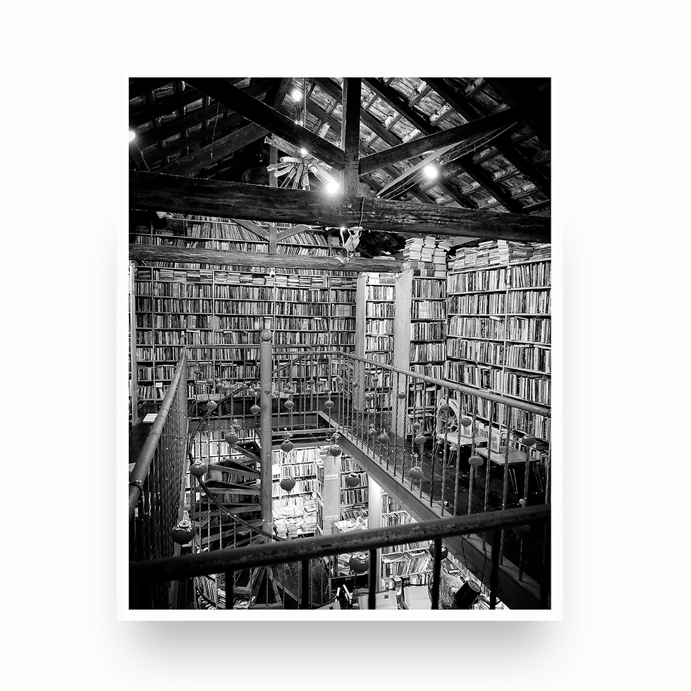 Thumbnail: Black and white photo looking down from the loft over bookshelves and spiral stairs at Nha Sach Mao.