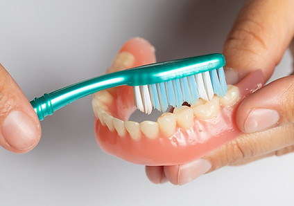 Person brushing lower dentures with a toothbrush.