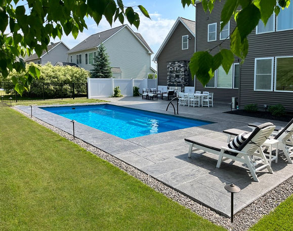 Rectangular in-ground swimming pool with a stamped concrete patio and pool deck and a house in the background.
