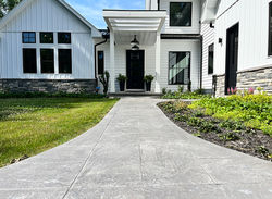 Long concrete walkway leading to a front door to a white house.