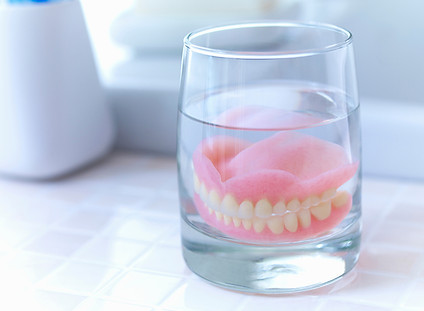 Dentures soaking in a glass of water.