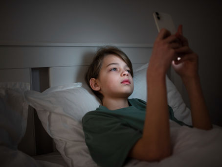 Criança, deitada numa cama, olhando o celular.