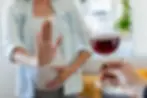 Imagem de uma mulher grávida fazendo sinal de 'pare' com a mão enquanto um copo de vinho é oferecido. Contexto de prevenção ao consumo de álcool na gravidez.