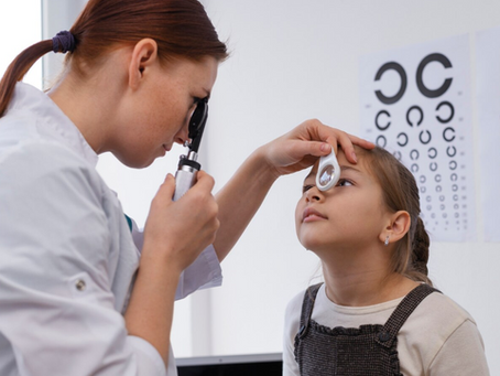 Criança sentada em um cadeira com a oftamologista examinando os olhos da criança com equipamento especializado