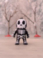 3D printed skeleton keychain figure with black base and white bones, posed in front of a soft-focus tree background.