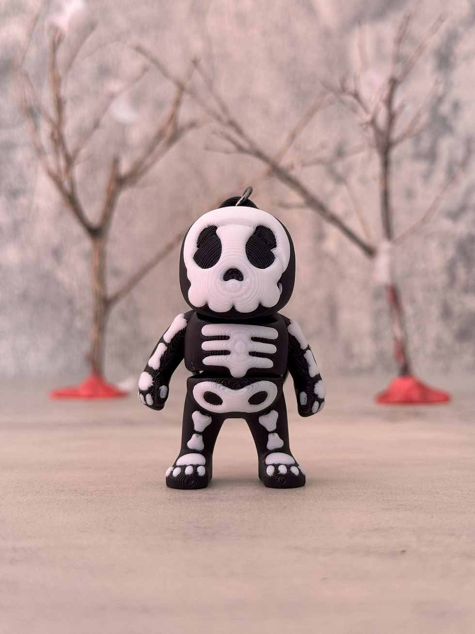 3D printed skeleton keychain figure with black base and white bones, posed in front of a soft-focus tree background.