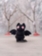 Cute 3D printed bat keychain figure with pink eyes and spread wings, displayed with a soft background and bare winter trees.