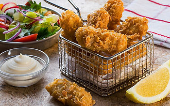 A basket of fried chicken with a bowl of mayonnaise and a slice of lemon on a table.