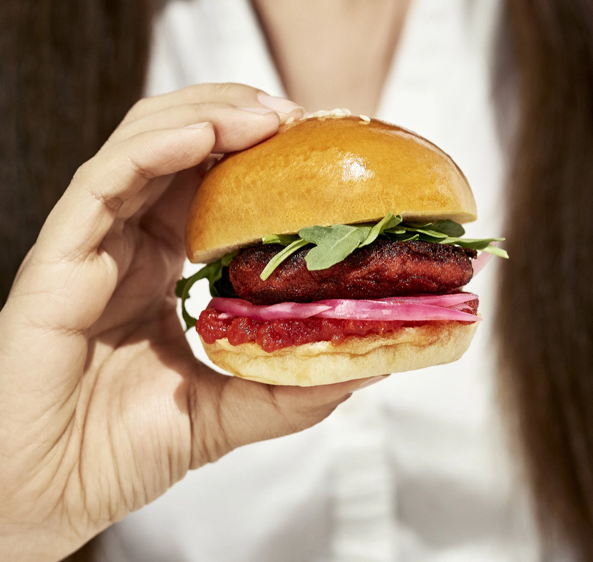 A photo of a cultivated meat hamburger sitting on a wooden table. The hamburger has a juicy beef patty, melted cheddar cheese, lettuce, tomato, and onion on a toasted sesame seed bun.