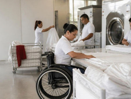 Trabajadores de una lavandería industrial, entre ellos una mujer en silla de ruedas, doblan sábanas blancas en Barranquilla.