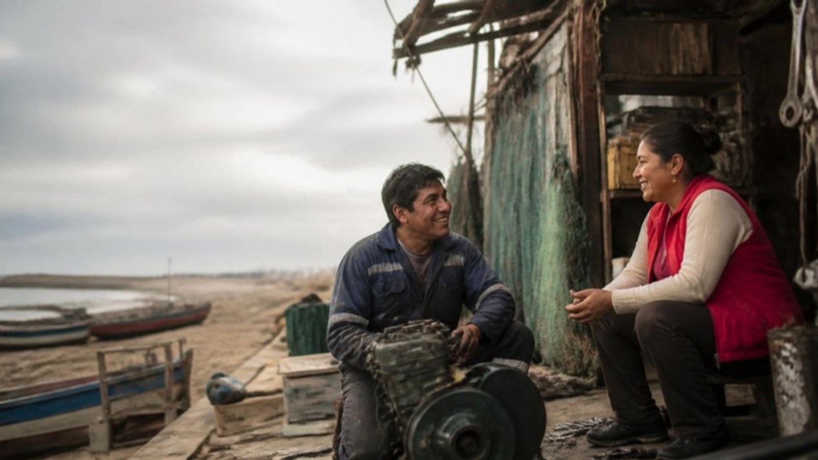 Mecánico de motores marinos y vendedora de insumos conversan frente a su taller en un muelle de pesca artesanal en Perú