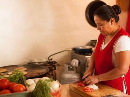 Cocinera de una fonda mexicana pica jitomate junto a una estufa de gas.