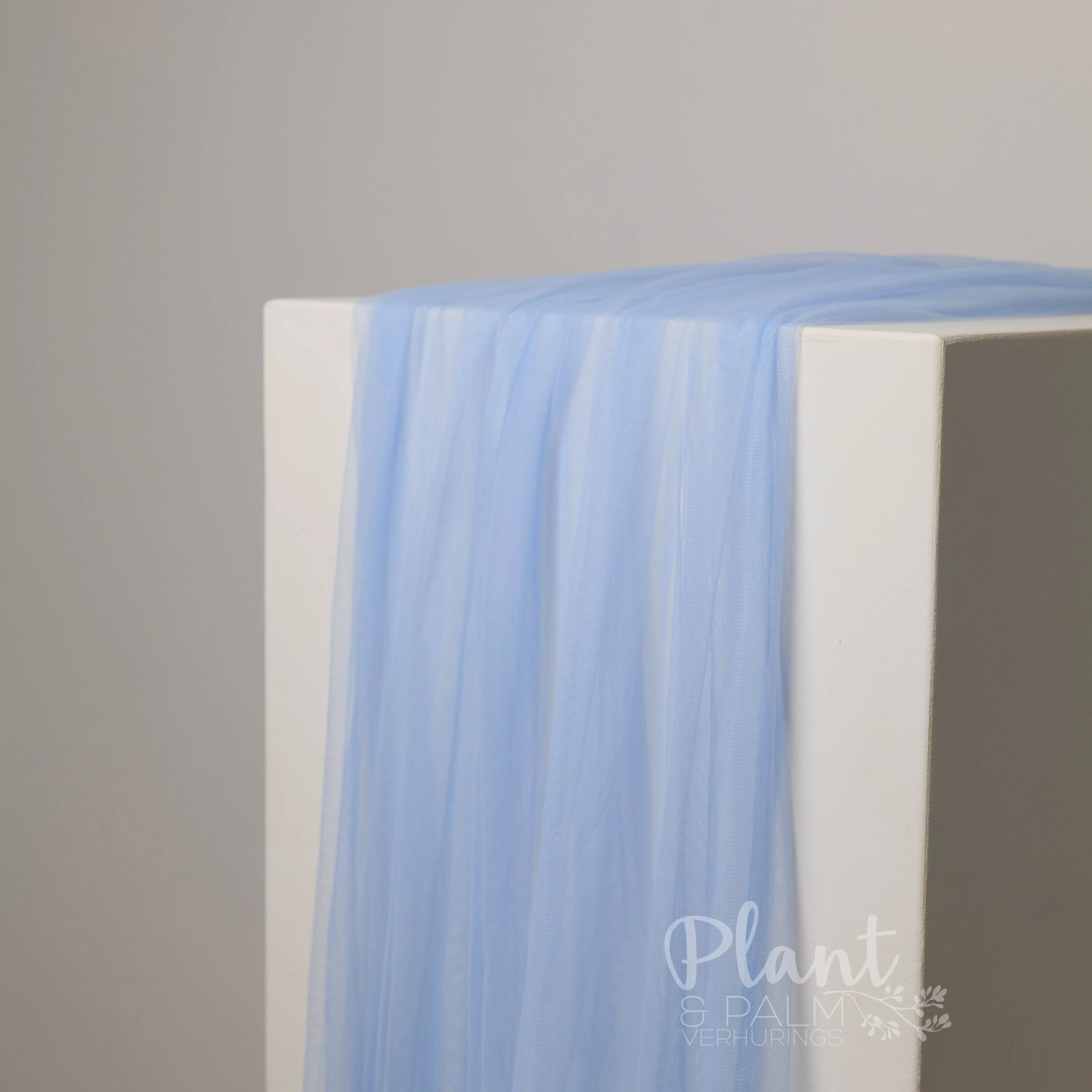 Light blue tulle table runner draped over a white display plinth
