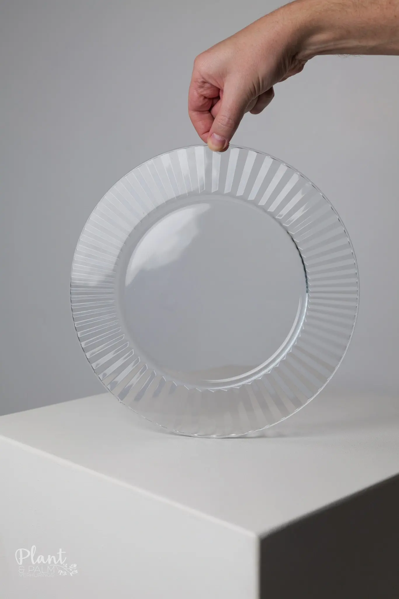Hand holding a clear ribbed glass underplate from Plant and Palm Rentals, ideal for weddings and table décor