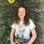 Molly holding a book in front of a brick wall, smiling