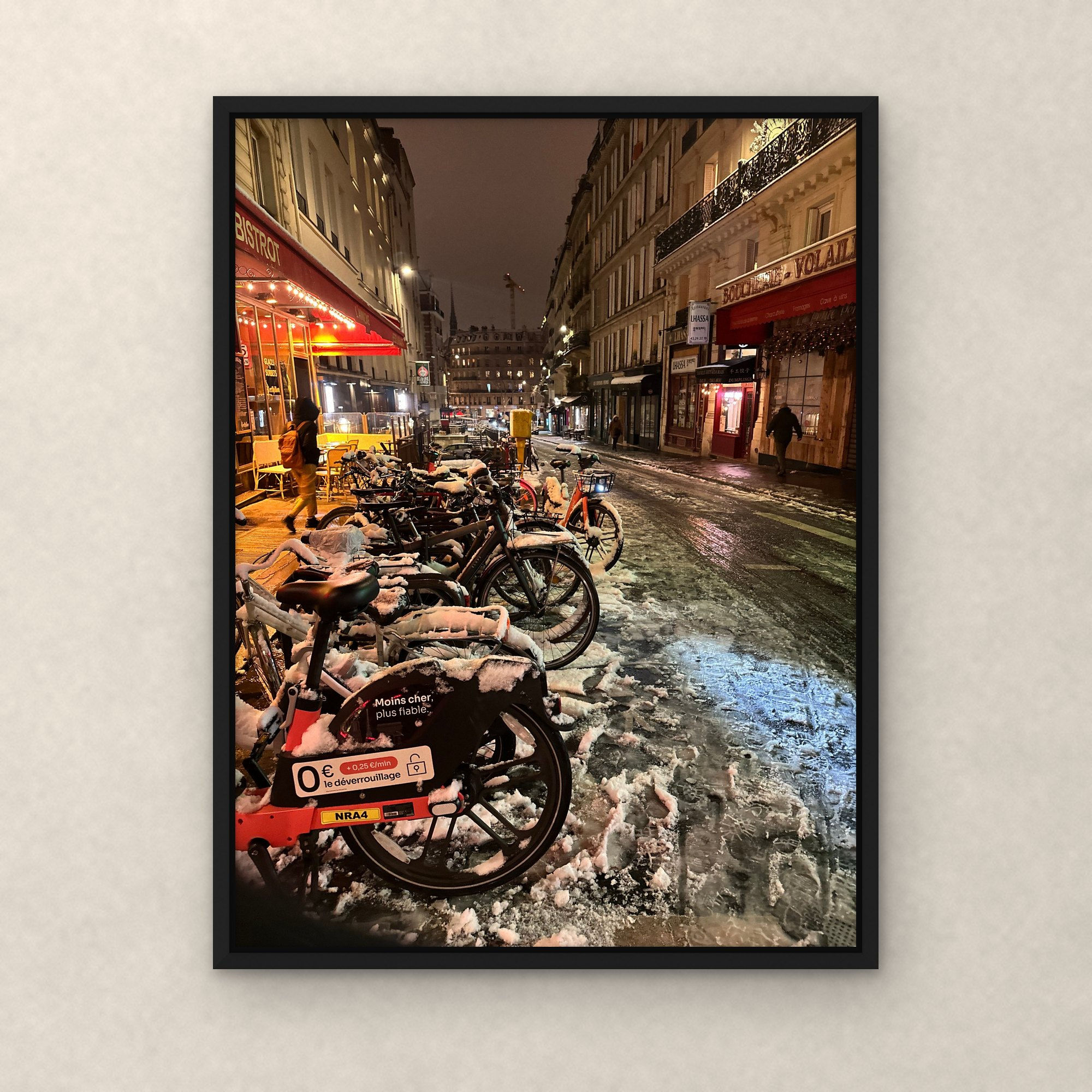 Bistrot in the Snow framed canvas in a black floating frame on a plaster wall