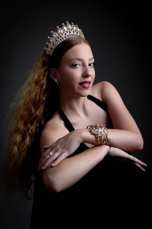 Portrait en studio d'une jeune femme souriante, les bras croisés au premier plan, arborant une couronne dorée et un bracelet.