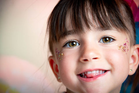 Macro et très gros plan serré du visage d'une petite fille souriante aux yeux noisette avec du maquillage pailleté sur les joues.