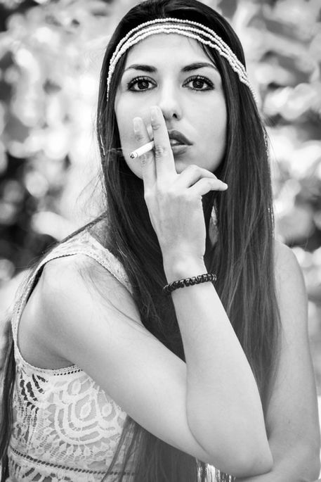 Portrait en noir et blanc d'une femme au style bohème avec un headband, tenant une cigarette en extérieur, shooting photo artistique en lumière naturelle.