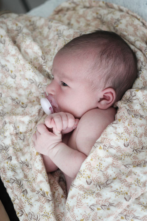 Bébé nouveau-né emmailloté dans un tissu doux et blanc lors de sa séance en studio.